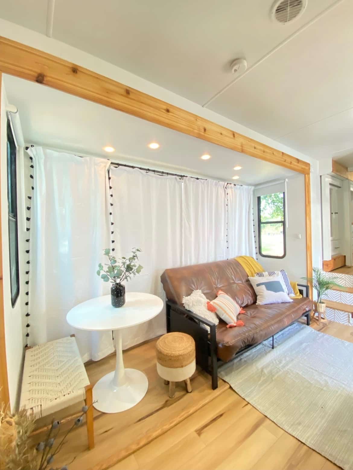 RV lounge with brown futon, white curtains, and small dining table.