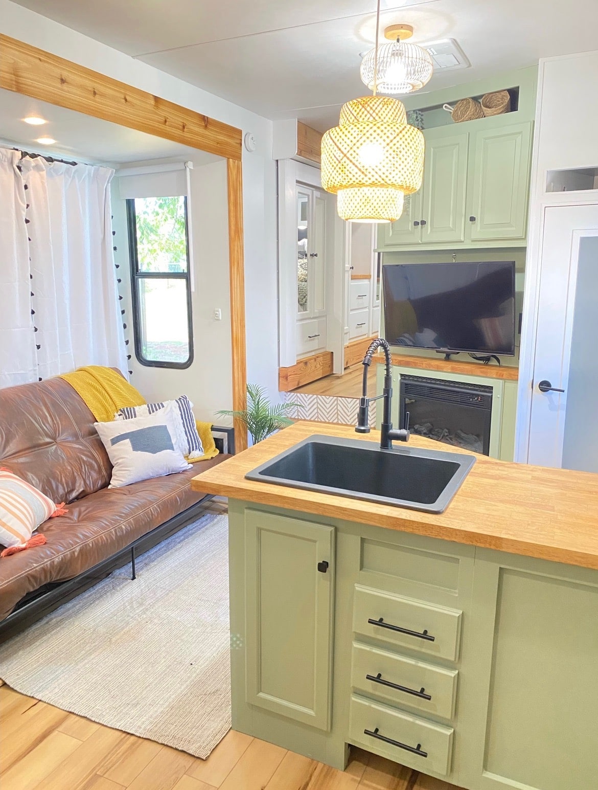 Open RV interior showing kitchen island, futon sofa, and TV with fireplace.