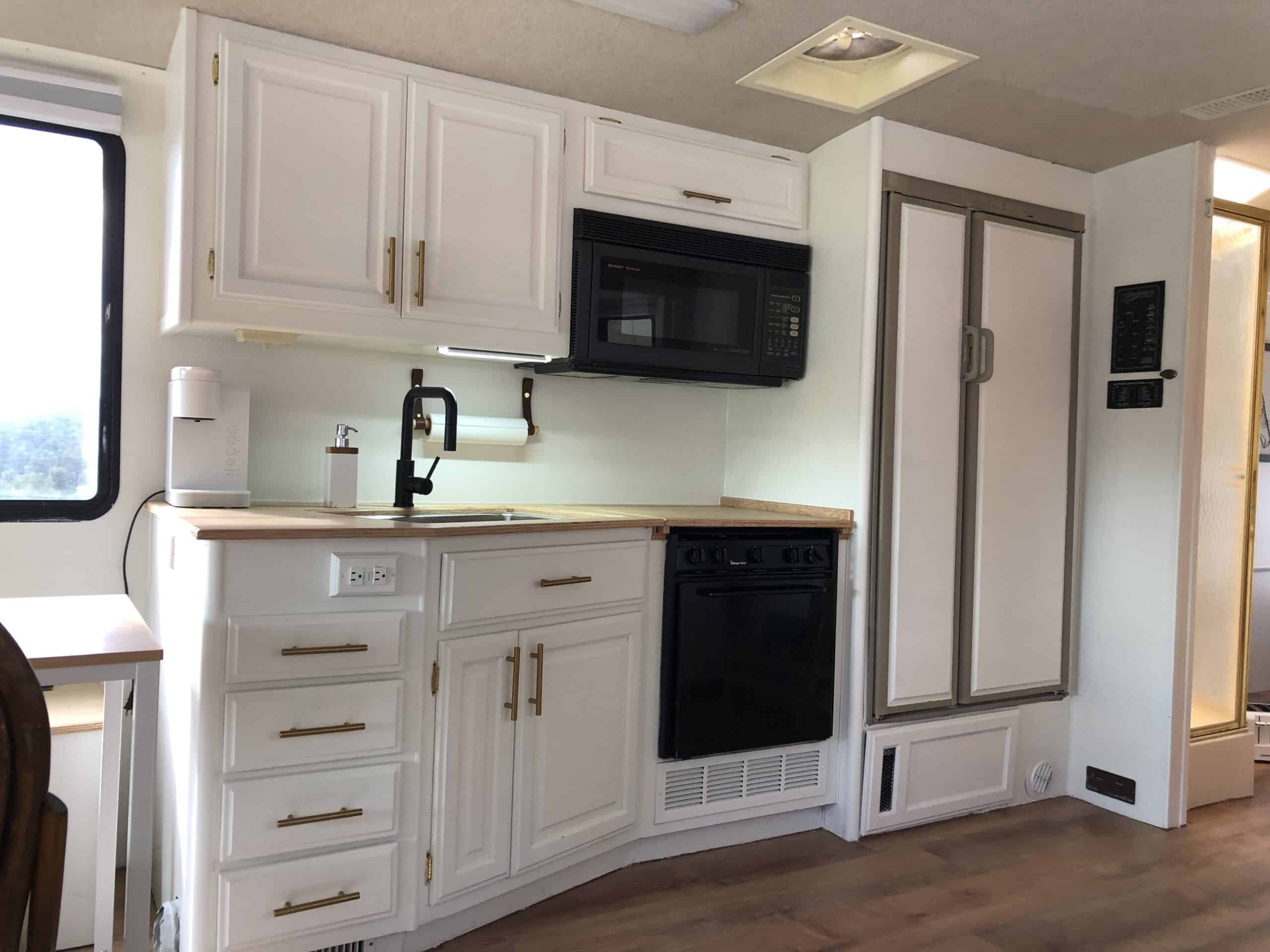 RV kitchen with white cabinets, wood countertop, and built-in appliances.