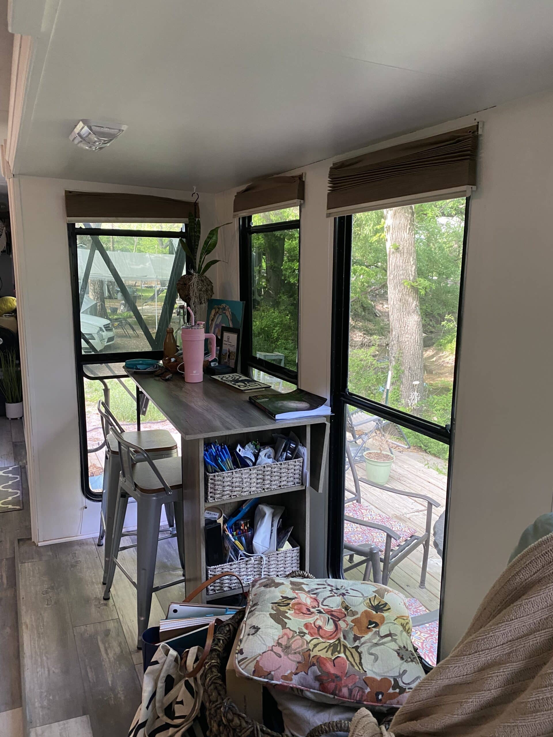 Bar-height table with stools in RV nook surrounded by windows and deck views.