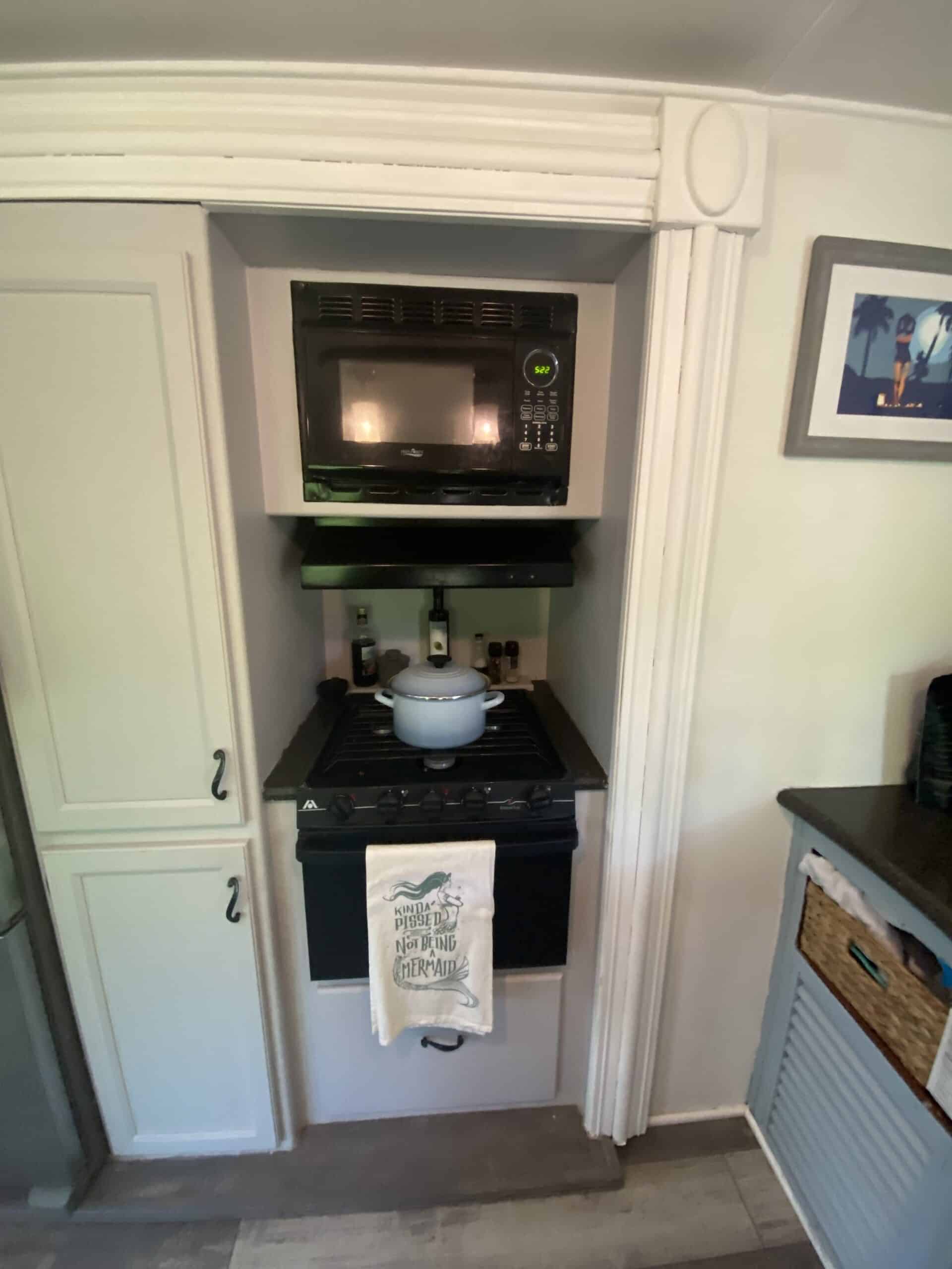 Close-up of RV cooking area with microwave, gas range, and white cabinets.