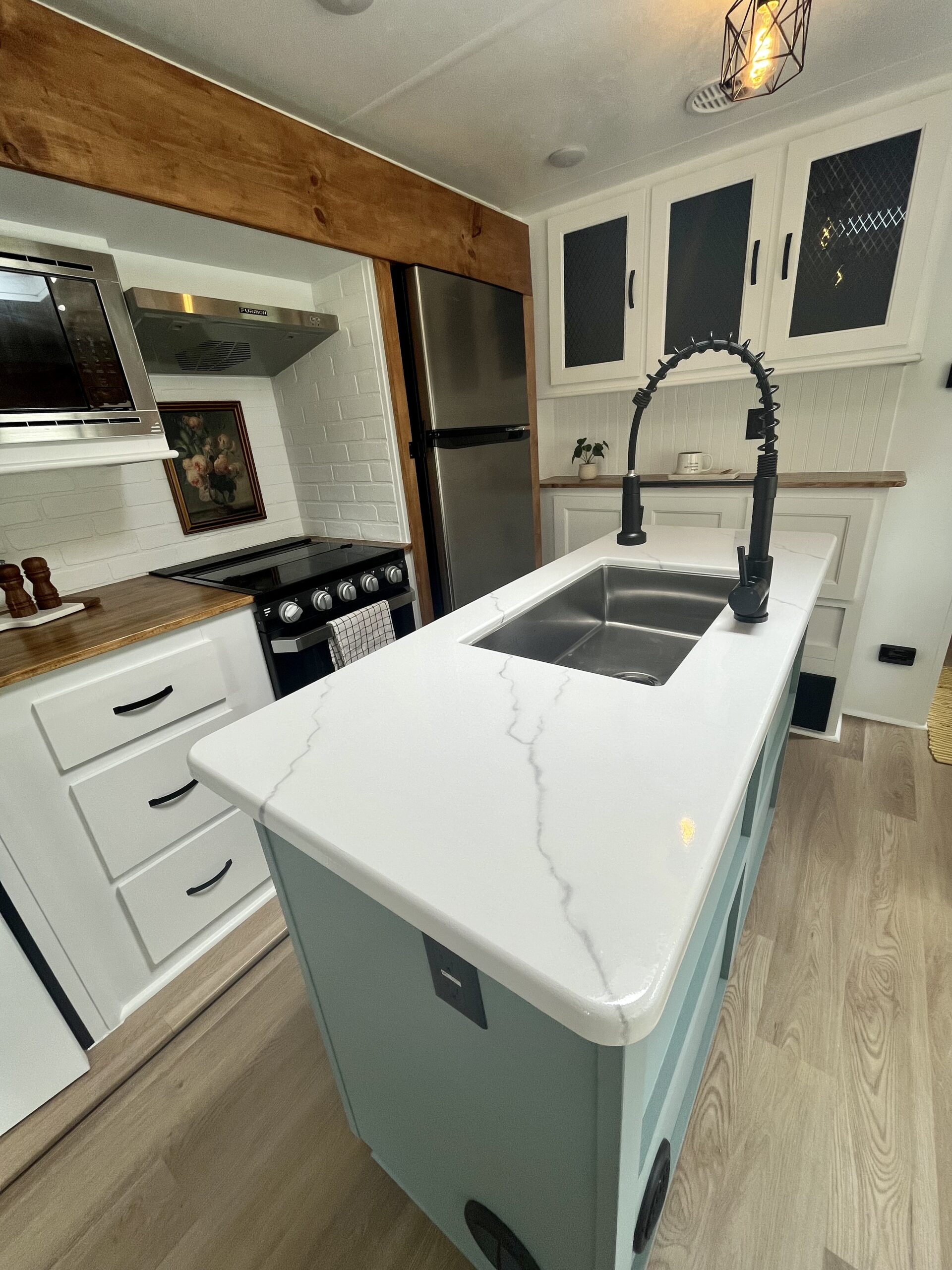 Renovated RV kitchen with center island, stainless appliances, and ample cabinet storage.