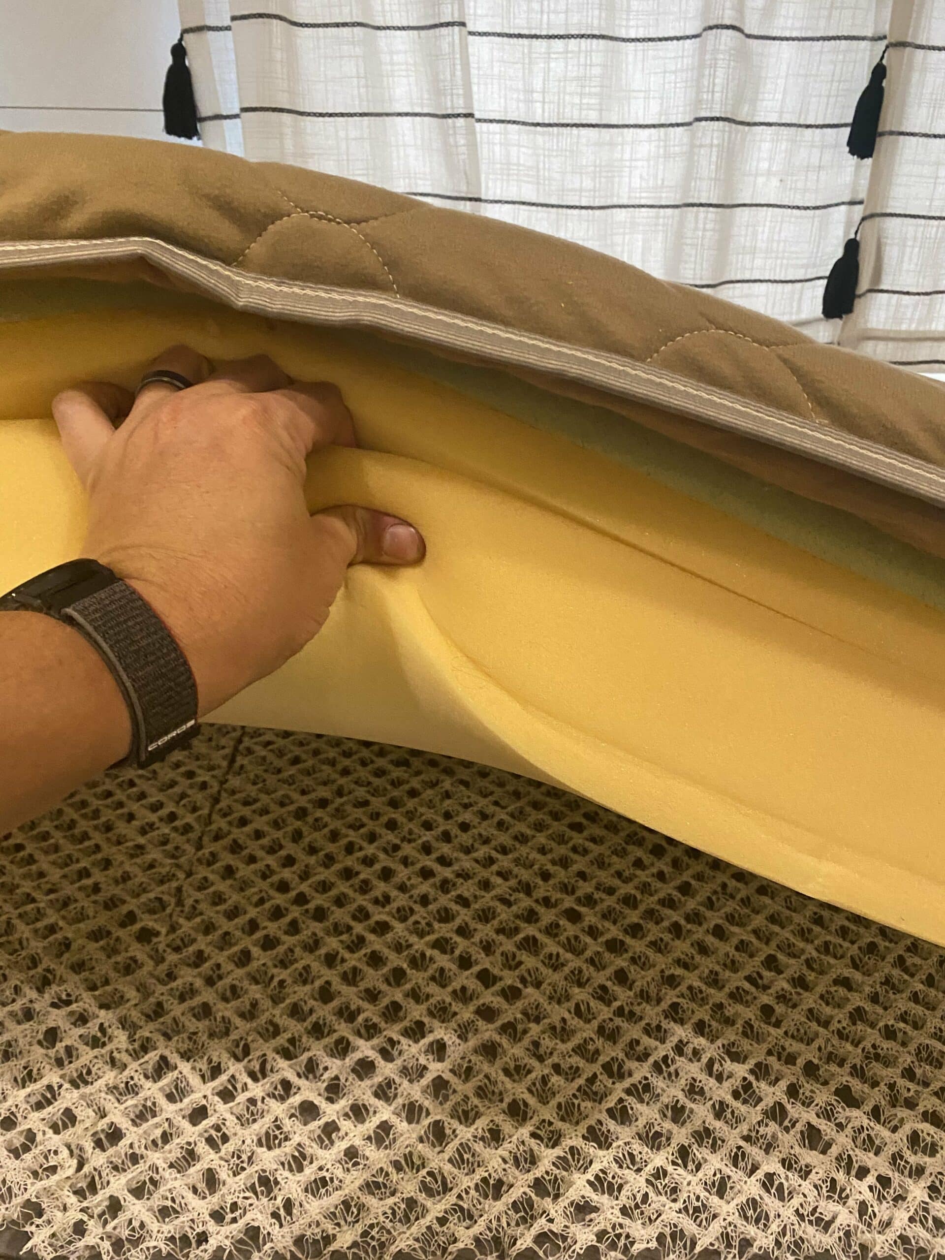Close-up of RV bed showing foam mattress lifted to reveal ventilated mesh underlay.
